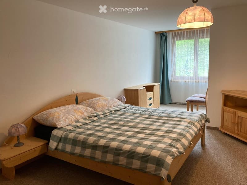 Bedroom with wooden bed, two pillows, wooden nightstands, wooden cabinet, desk, chair, window with curtains, lamp