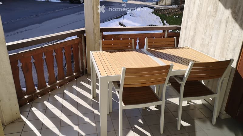 Balcony with table and chairs, tiled floor, wooden railing, view of street and snow