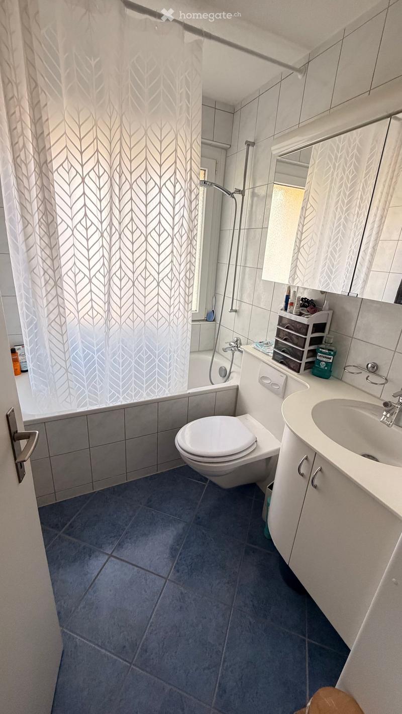 Modern bathroom with blue tiles, white fixtures, a toilet, sink, bathtub, and a shower area with a curtain.