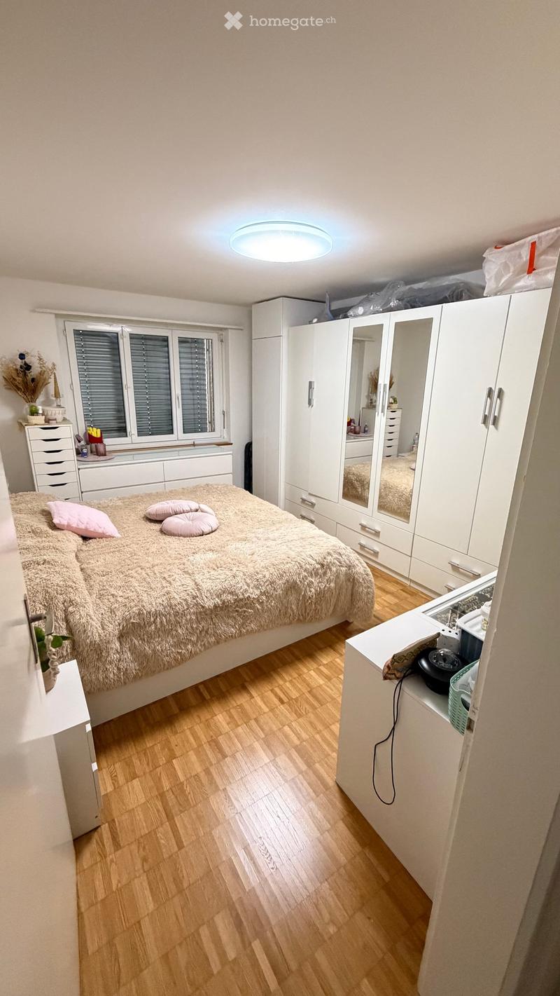 A well-lit bedroom with a large bed, a wardrobe with mirrored doors, a sink, and a small table with a chair.