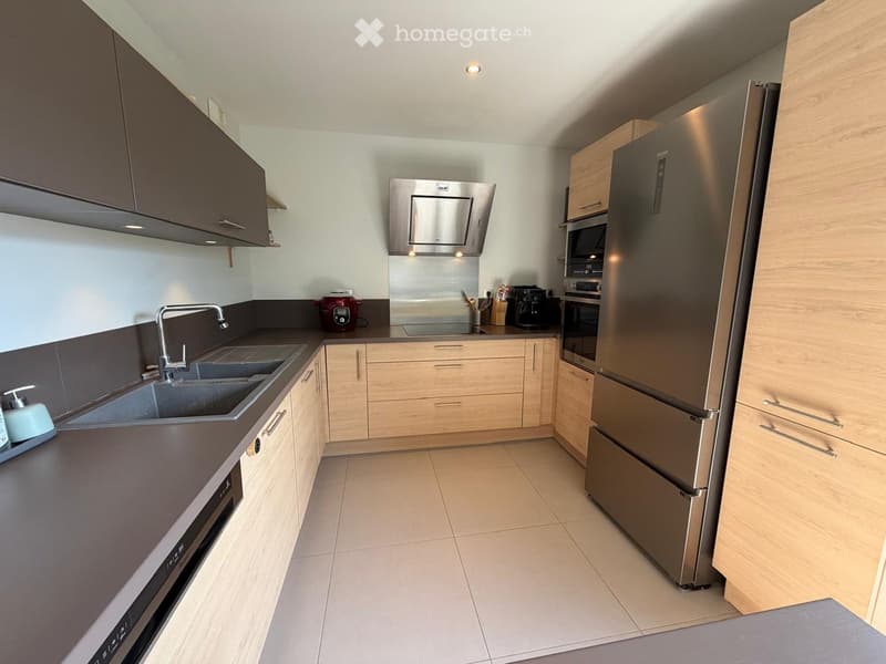 Modern kitchen with light wood cabinets, stainless steel appliances, and a double sink.