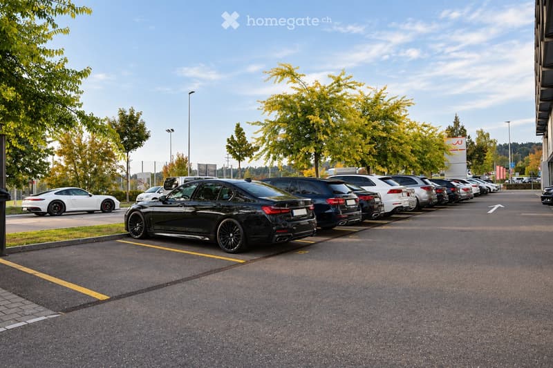 Parking lot with several parked cars, trees, and a building in the background.