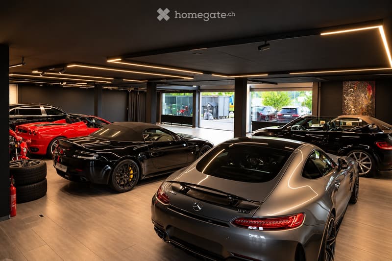 Modern car showroom with several luxury cars, including a convertible, a sports car, and a motorcycle, displayed on a polished wooden floor. The space features sleek lighting and large windows allowing natural light to enter.