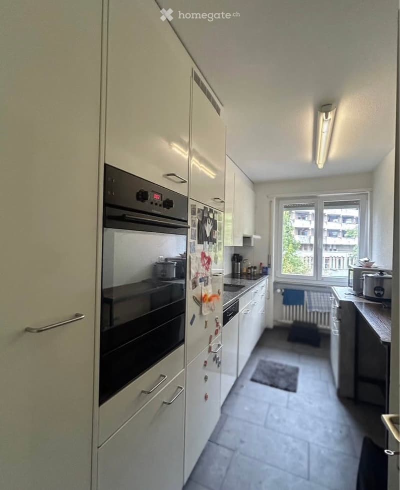 Modern kitchen with white cabinets, stainless steel appliances, and a large window offering a view of the city.