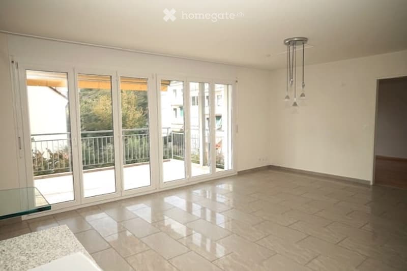 Empty room with large sliding glass doors leading to a balcony, tiled floor, and a glass side table near the entrance.