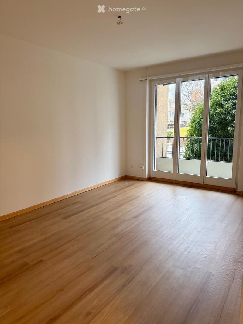 Empty room with light wooden flooring, white walls, and large sliding glass doors leading to a balcony.