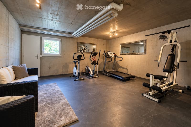Well-lit fitness room with a sofa, exercise bike, treadmill, weight machine, mirrors, and a window.