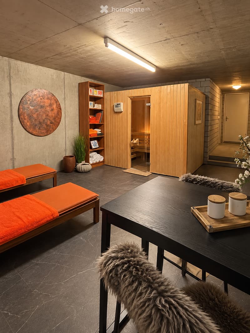 Spa or relaxation room with wooden sauna, benches, a table with cups, a shelf with towels, and decorative items.