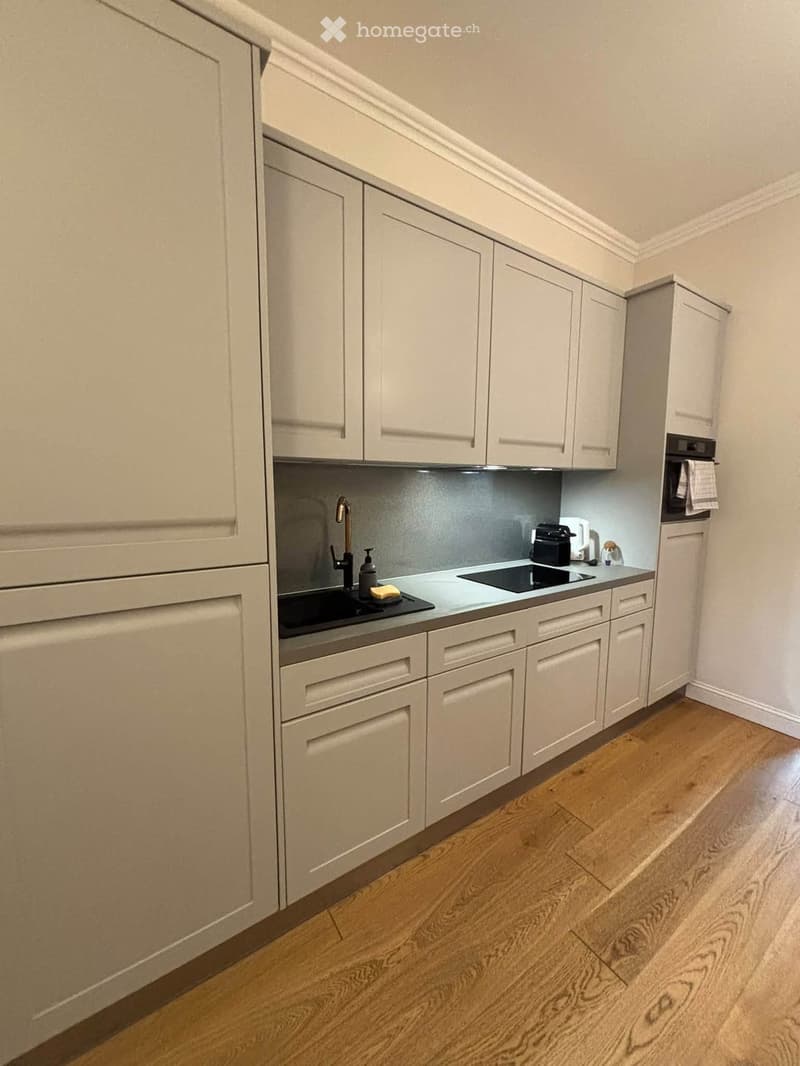 Modern kitchen with light-colored cabinets, a stainless steel sink, and a wooden floor.