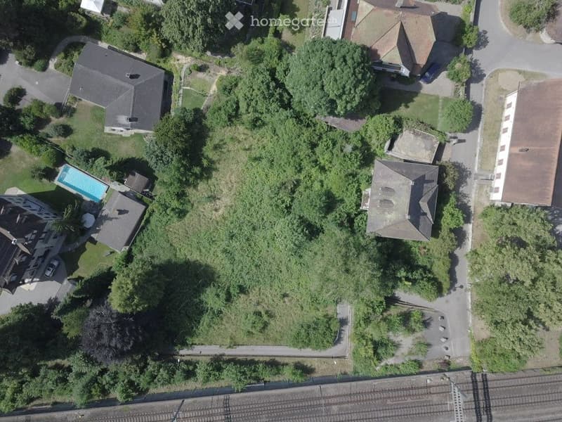 Aerial view of a residential area with multiple houses, a swimming pool, and surrounding greenery.