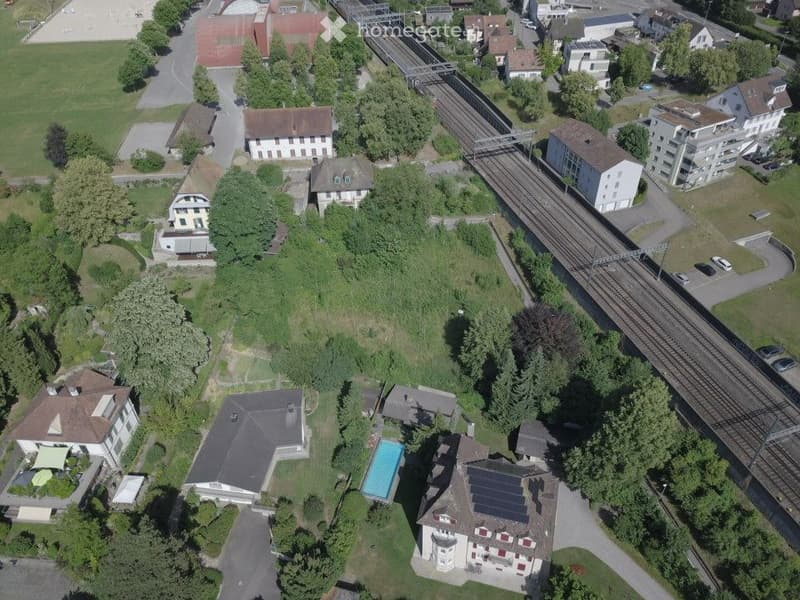 Aerial view of a residential area with multiple houses, a swimming pool, and a train track running through the neighborhood.