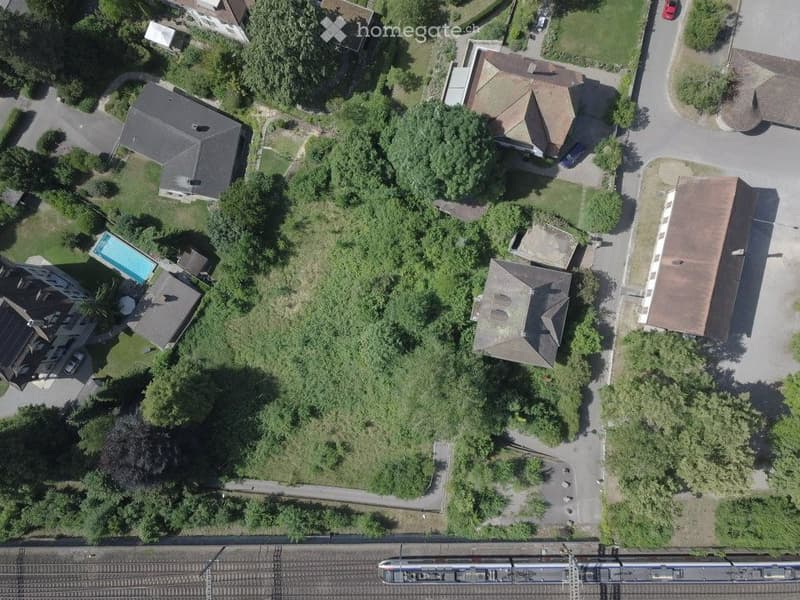 Aerial view of a residential area with multiple houses, a swimming pool, and surrounding greenery.