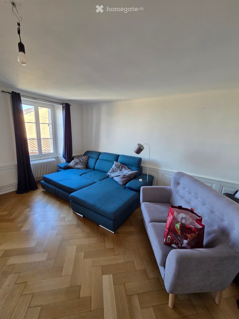 Living room with a blue sectional sofa, grey armchair, floor lamp, and wooden flooring.