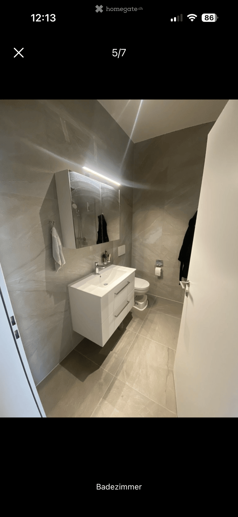 Modern bathroom with a white sink, mirror, toilet, and towel, featuring sleek, contemporary design and neutral tones.