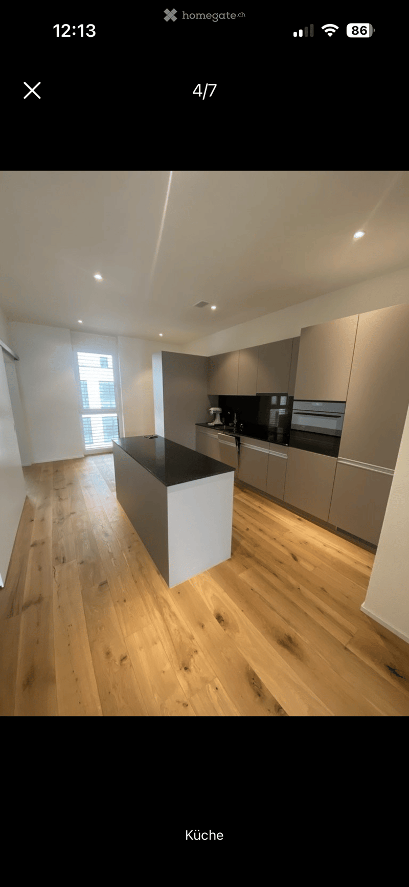 Modern kitchen with wooden flooring, black countertop, grey cabinets, and stainless steel appliances including an oven and sink.