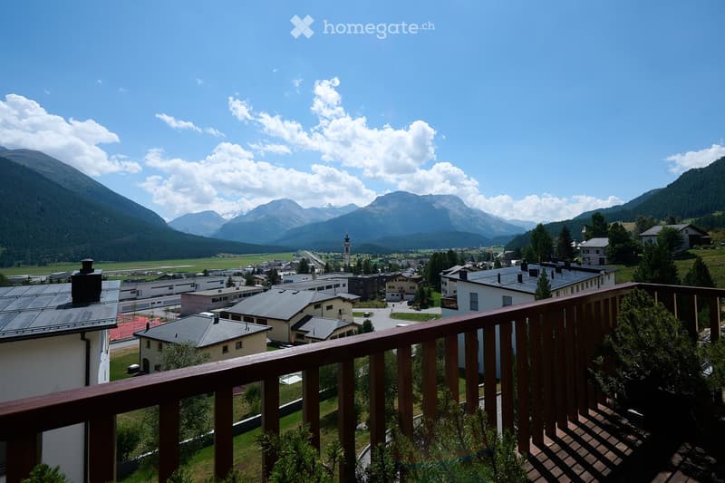 Balcony overlooking a scenic valley with mountains, houses, and a church in the distance.