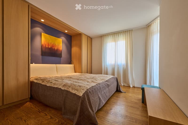 Modern bedroom with a large bed, fur throw, wooden floor, large window with curtains, and a painting on the wall.
