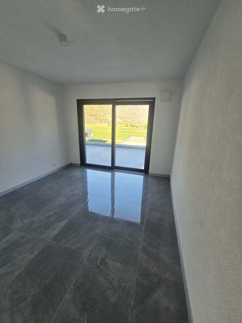 Empty room with dark tiled floor, white walls, and large sliding glass door leading to outdoor area with pool and landscape.