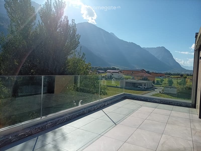 A modern balcony with a glass railing, tiled floor, and scenic mountain view.