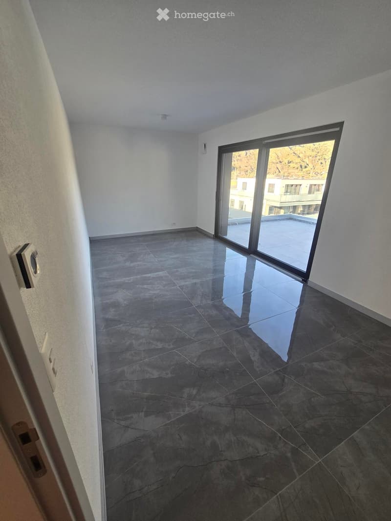 Empty room with dark grey tiled floor, white walls, and large sliding glass door leading to a balcony.