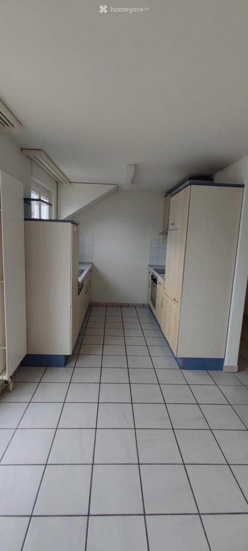 Empty kitchen with tiled floor, white cabinets, and built-in appliances, but no furniture or items present.