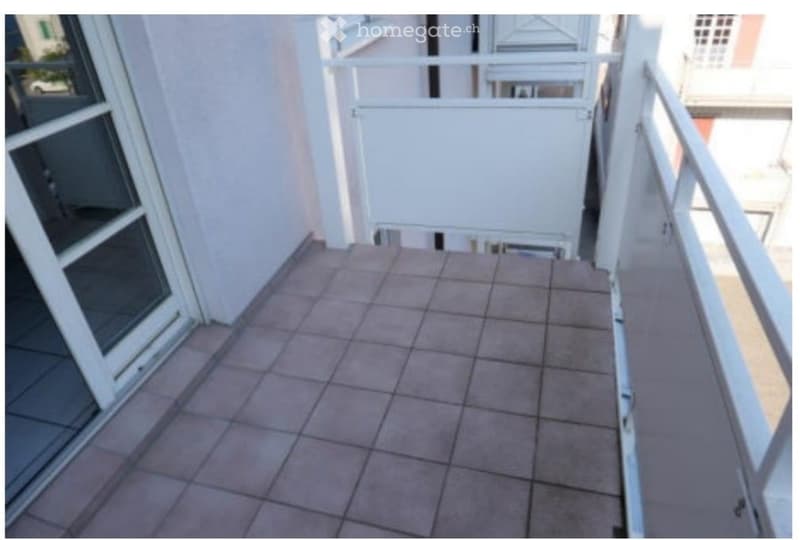 Balcony with tiled floor, white metal railing, and glass door leading to the interior.