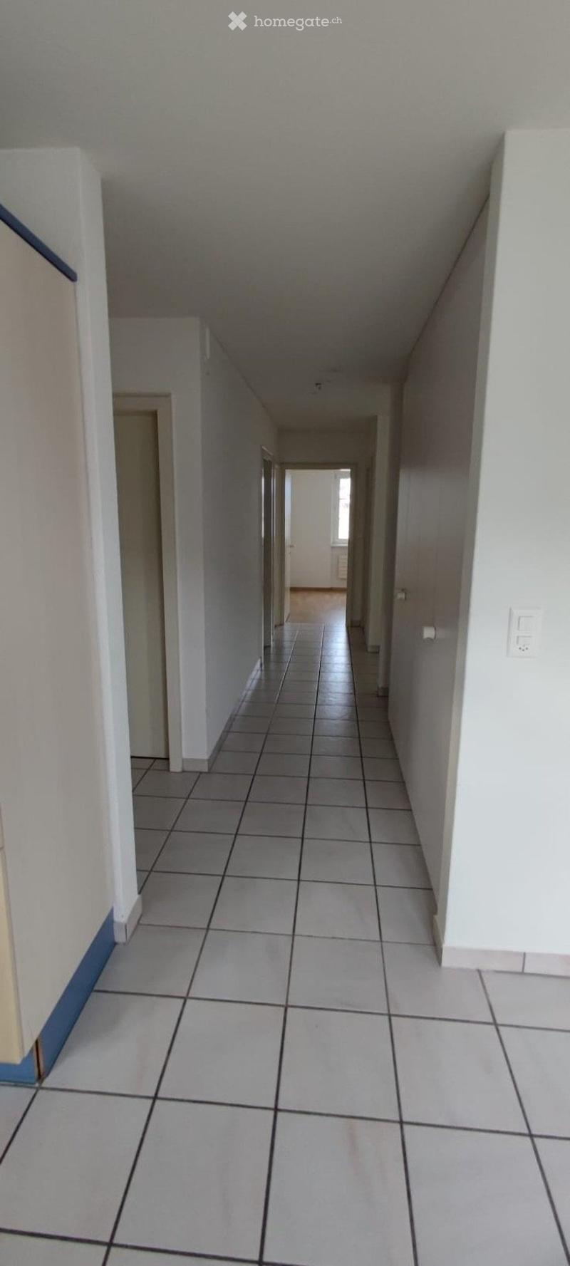 Empty hallway with tiled floor and white walls, leading to an open doorway at the end.