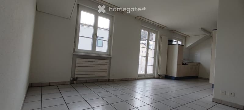 Empty room with tiled floor, large windows, radiator, and small built-in cabinet with sink.