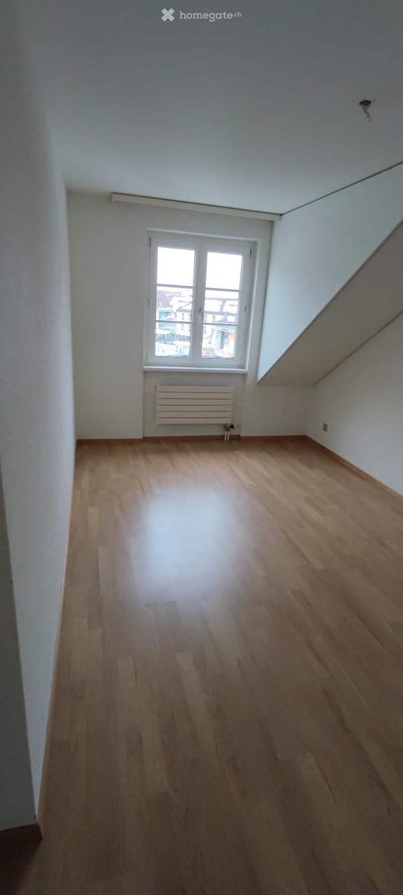 Empty room with wooden flooring, white walls, and a window with a radiator below it.