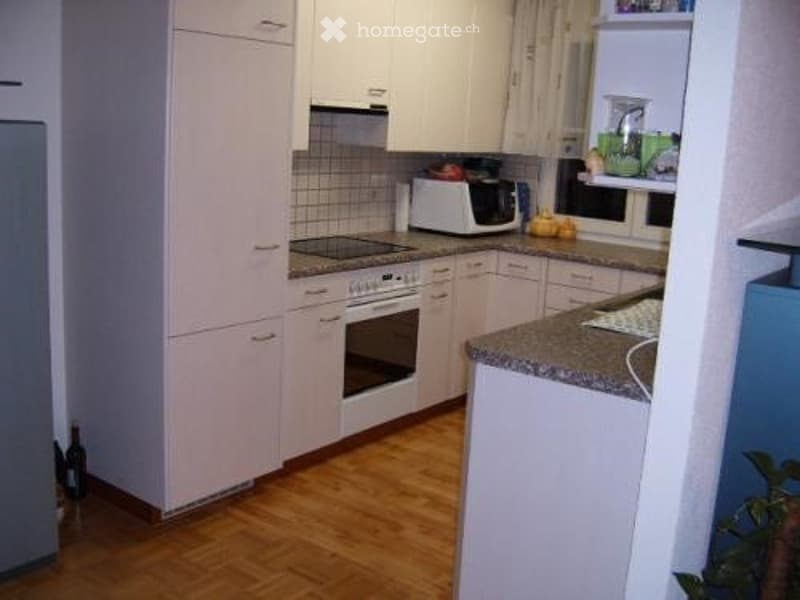 Bright kitchen with white cabinets, wooden flooring, and modern appliances including an oven, microwave, and refrigerator. Countertop features a faucet and some small items.