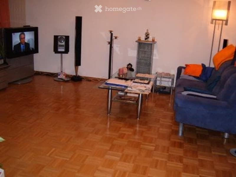Living room with wooden flooring, blue sofa, coffee table, television, and floor lamp.
