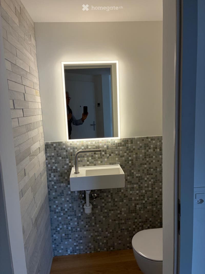 compact bathroom with modern tile design, wall-mounted sink, mirror with lighting, and a toilet