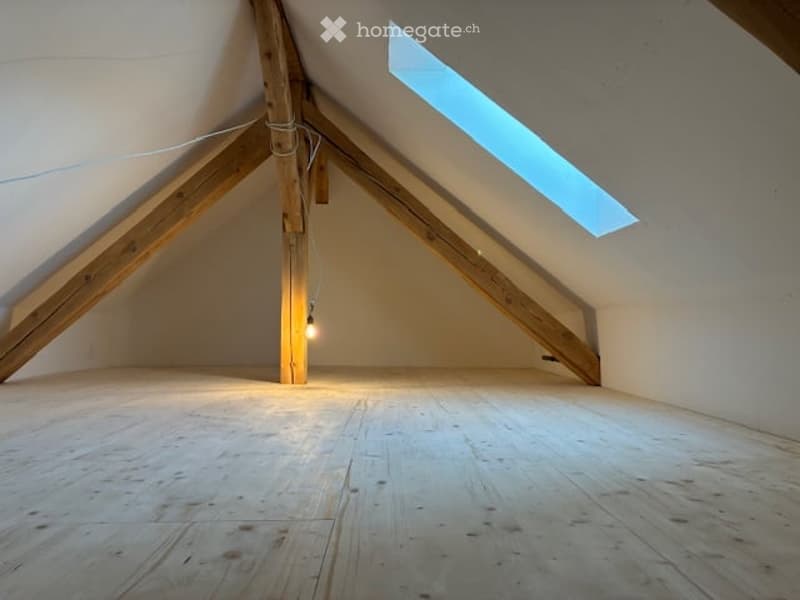 Empty attic space with wooden beams, exposed wooden floor, and a skylight window allowing natural light.