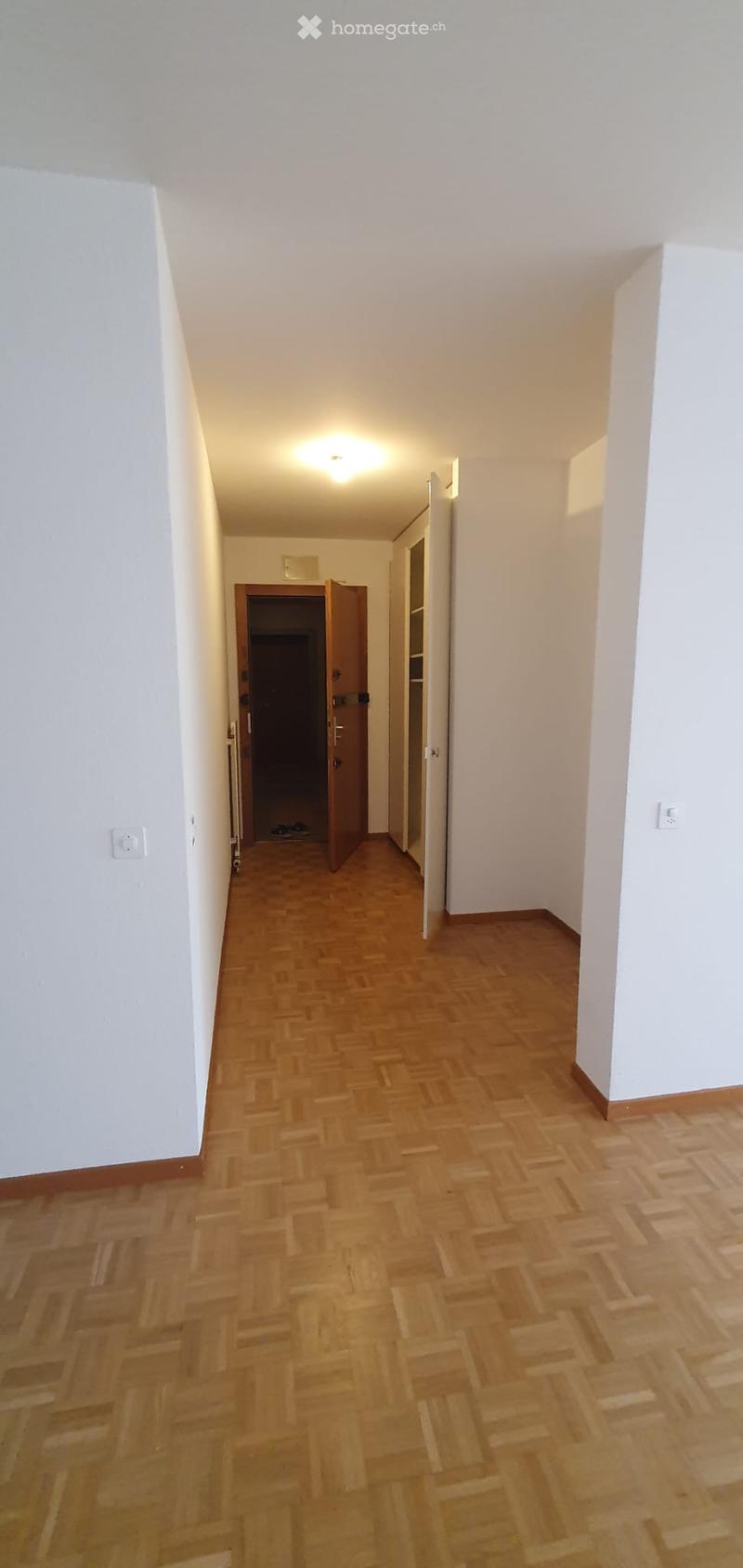 Empty hallway with wooden flooring, white walls, and recessed lighting. Open doors lead to adjacent rooms.