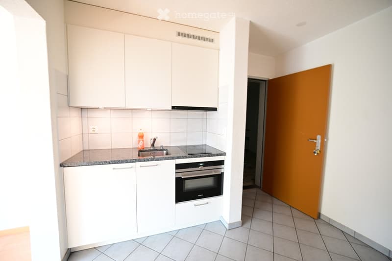 Modern kitchen with white cabinets, granite countertop, built-in oven, and a sink with a faucet. A bottle is placed on the counter.