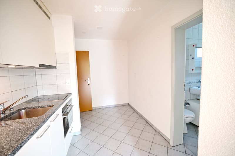 Modern kitchen with white cabinets, granite countertop, stainless steel sink, and faucet. Adjacent bathroom features a toilet, bathtub, and sink.