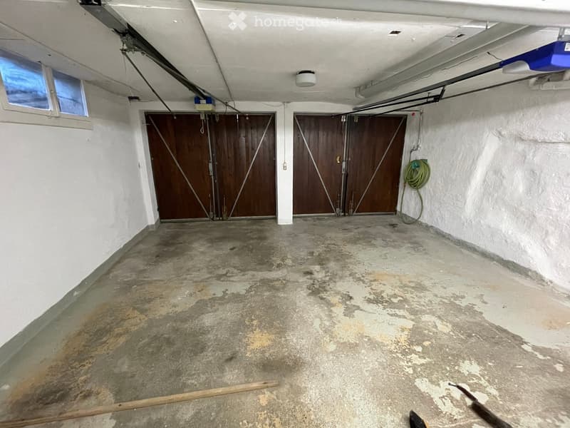 Empty garage with concrete floor, two large wooden garage doors, and a small window on the left side.