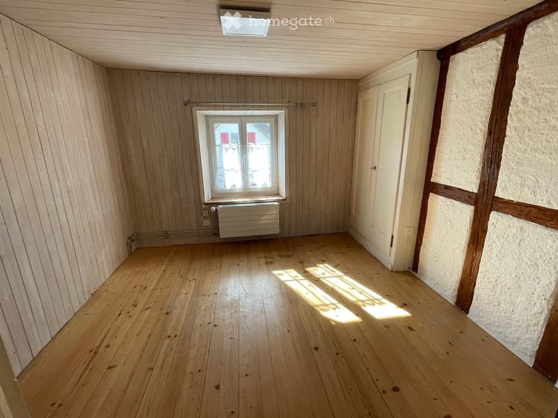 Empty room with wooden flooring, wooden walls, a window with white frame, and a white door.