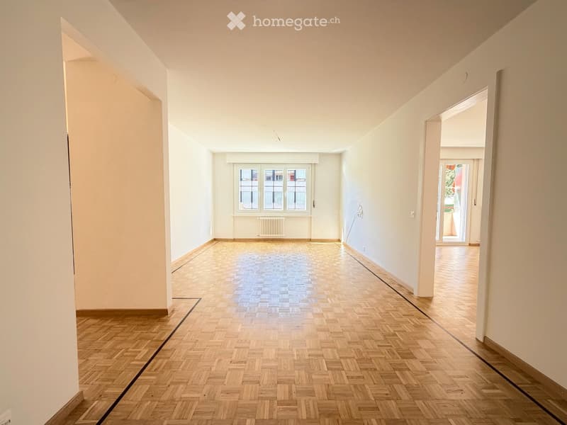 Empty hallway with wooden herringbone flooring, white walls, and large windows allowing natural light. No furniture or equipment present.