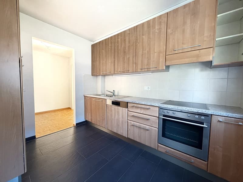 Modern kitchen with light wooden cabinets, granite countertop, stainless steel oven, dishwasher, and sink.