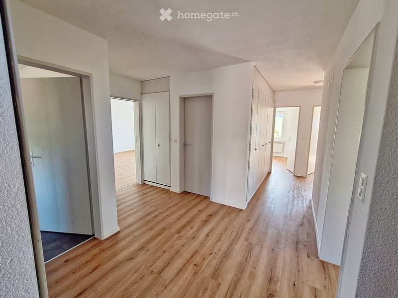 Empty hallway with wooden flooring, white walls, and several doors leading to other rooms.