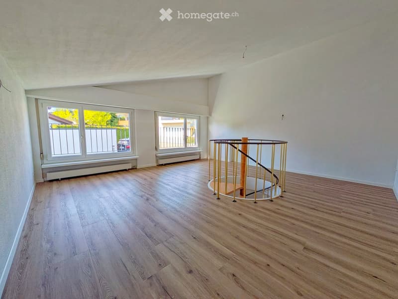 Empty room with wooden flooring, white walls, large windows, and a modern spiral staircase with a glass railing.