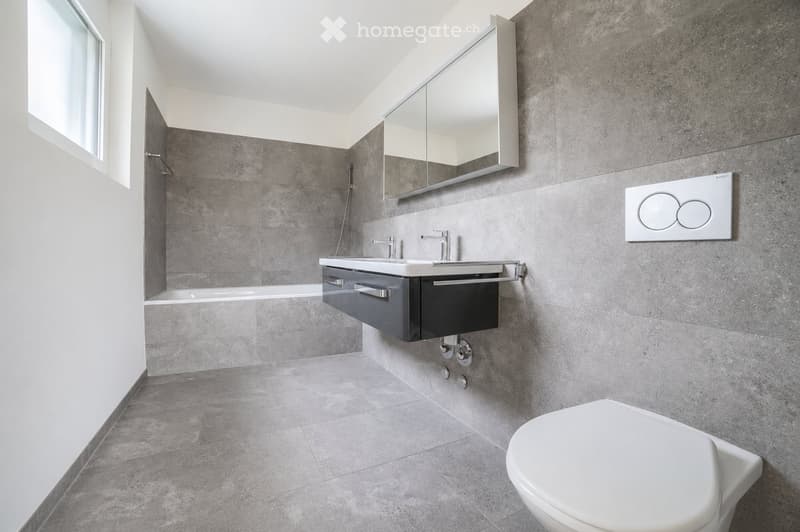 Modern bathroom with grey tiles, a double sink, a large mirror, and a toilet.
