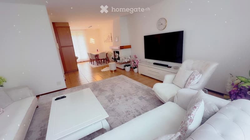 Modern living room with white leather sofa, armchair, coffee table, TV, fireplace, dining area with table and chairs, and decorative flower pots.
