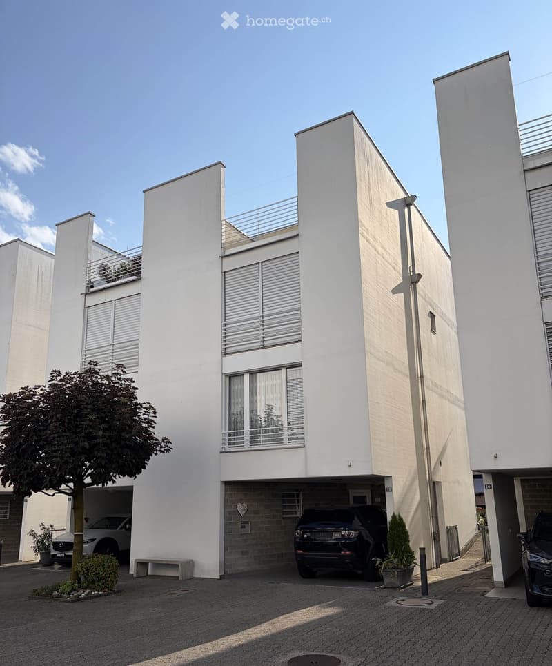 Modern two-story white building with balconies, garage, and parking area.