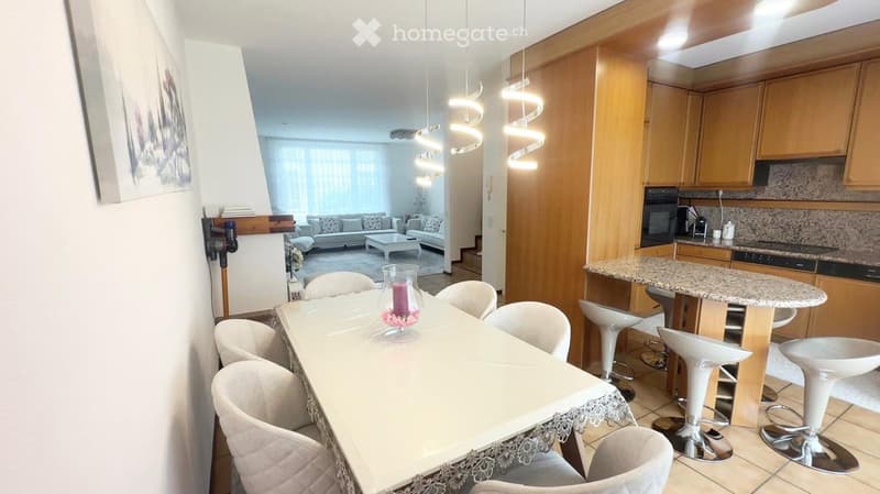Open-concept living and dining area with a dining table, chairs, sofa, coffee table, and a kitchen island with stools. The kitchen features wooden cabinets, granite countertops, and stainless steel appliances.
