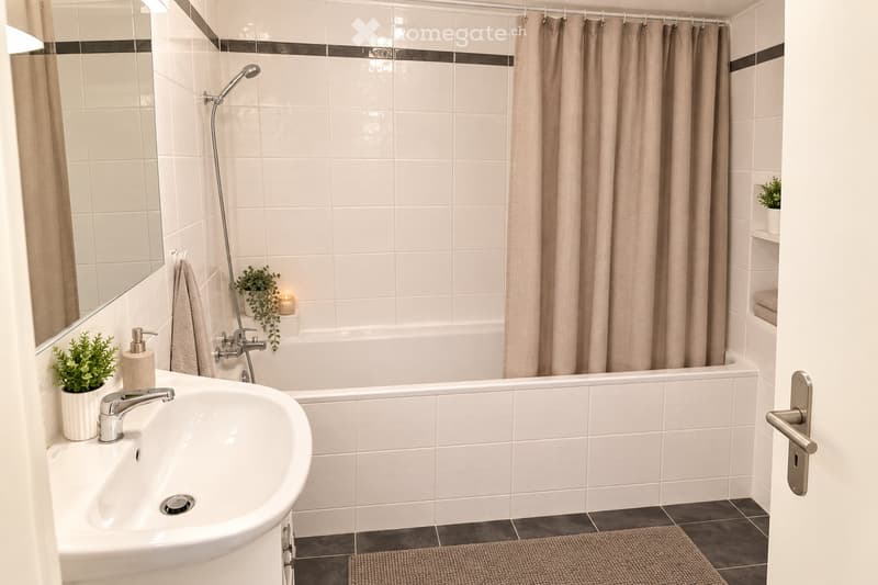 Modern bathroom with white tiles, a bathtub with a showerhead, a sink with a faucet, a mirror, and a small plant on the windowsill.