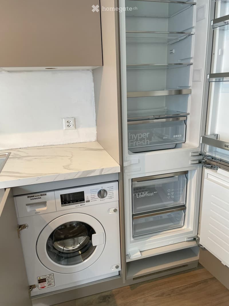 Compact kitchen area featuring a white Siemens washing machine and a white refrigerator with glass doors labeled "hyperFresh" and "LowFrost".