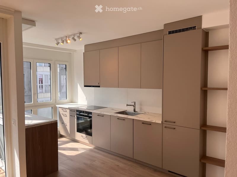 Modern kitchen with light-colored cabinets, a central island, and built-in appliances including an oven and sink.