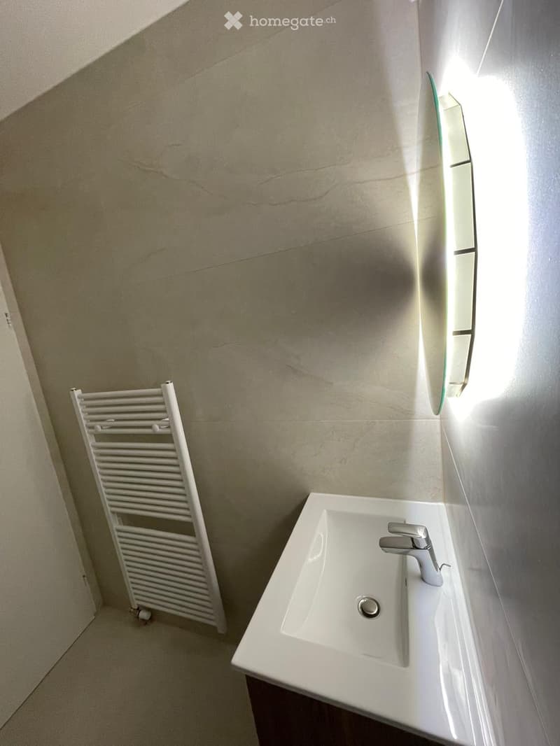 Modern bathroom with a white sink, chrome faucet, a white radiator, and a large mirror on the wall.